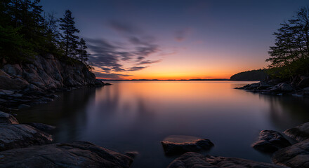 Serene Sunset over Calm Lake with Rocky Shores and Silhouetted Trees