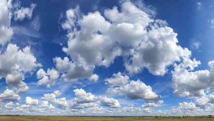 Wide expanse of a vibrant blue sky dotted with fluffy white clouds, a flat landscape below