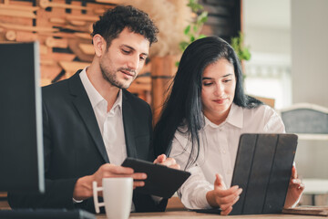 Two business professionals in office loft style using digital tablets discussing or meeting. Hispanic man and woman collaborating on work project. small business, lifestyle working in home office