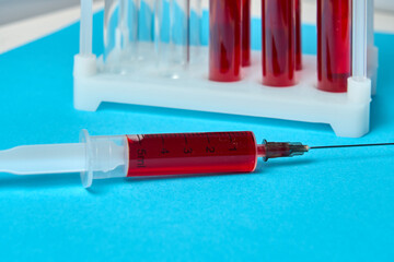 A syringe with a red liquid in it is on a blue surface. The syringe is labeled with the letters JL