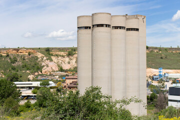 Four industrial silos rising above a quarry landscape under a blue sky