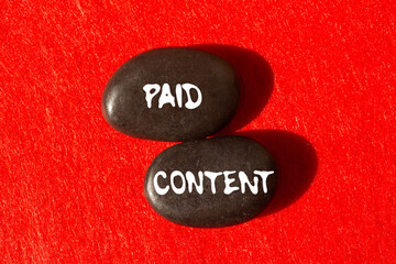 Paid content message written on black stones on red background. Conceptual paid content symbol....