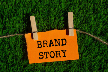 Brand story message written on ripped torn orange paper piece on green grass background. Conceptual...