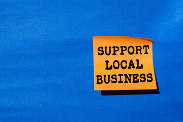 Support local business message written on orange paper on blue background. Conceptual support local...
