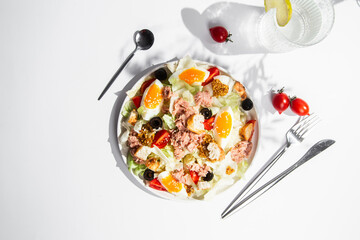 Appetizing Salad with iceberg, tuna, boiled eggs in a white plate on the table. Healthy breakfast