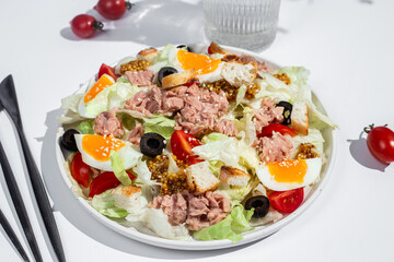 Appetizing Salad with iceberg, tuna, boiled eggs in a white plate on the table. Healthy breakfast