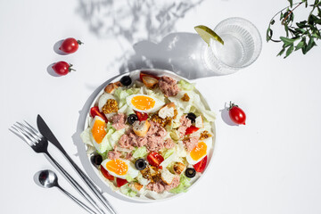 Appetizing Salad with iceberg, tuna, boiled eggs in a white plate on the table. Healthy breakfast