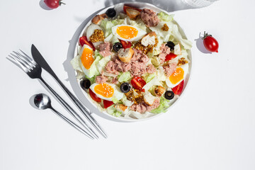 Appetizing Salad with iceberg, tuna, boiled eggs in a white plate on the table. Healthy breakfast