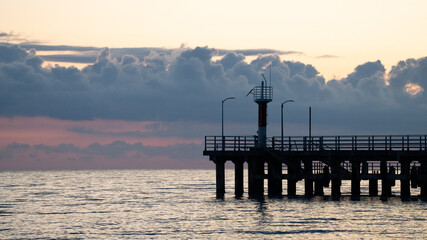 Silhouette of a Pier with Lighthouse at Sunset — Dramatic Sky over Calm Sea