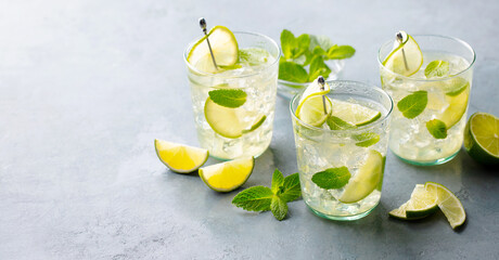 Mojito, Gin fizz cocktail with lime and mint, lemonade, ice tea in glass. Grey stone background....