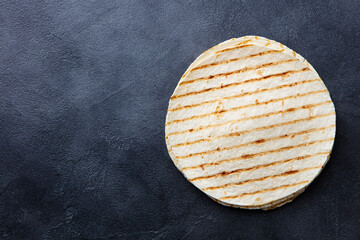 Grilled tortilla, lavash, flat bread on dark grey texture background. Copy space. Top view.