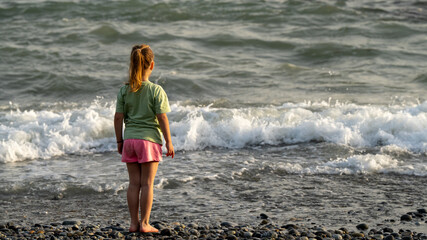 Girl Watching the Waves on a Pebble Beach — Childhood Moment of Wonder by the Sea
