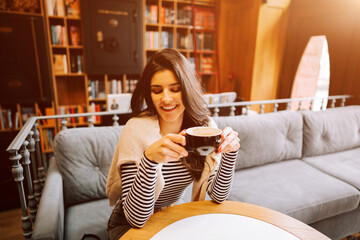 Woman enjoying coffee in cozy cafe surrounded by books in afternoon light
