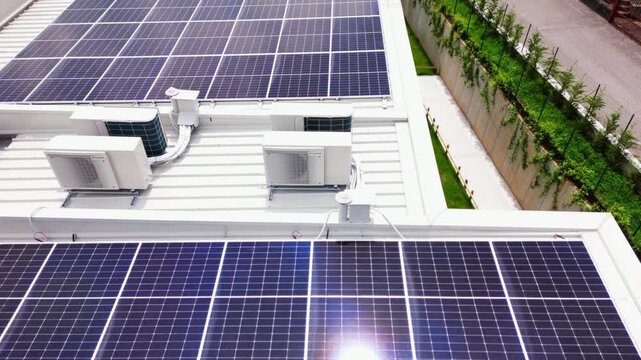 Low-pass drone view shows photovoltaic modules and HVAC condensers on white roof beside lush retaining wall and street. Lombardy, Italy Lombardia, Italia