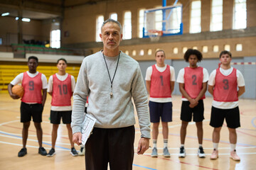 Basketball coach holding clipboard and coaching players in gymnasium