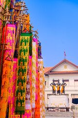 A vibrant display of traditional Lanna flags (Tung) in various colors, rising against a clear blue sky, part of a cultural festival in Northern Thailand.