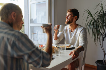 Gay couple enjoying breakfast and coffee together at home