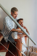 Fototapeta premium Tattooed gay couple embracing and smiling on stairs at home