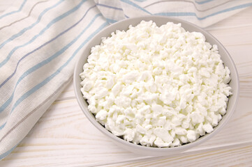 Farm cheese in a bowl on a light wooden background.