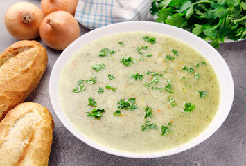 Homemade cream soup with chicken and herbs in a white plate on a gray background.