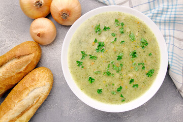 Homemade cream soup with chicken and herbs in a white plate on a gray background.