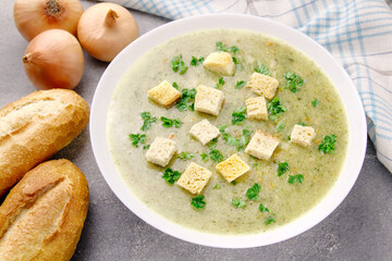 Homemade cream soup with chicken and herbs in a white plate on a gray background.