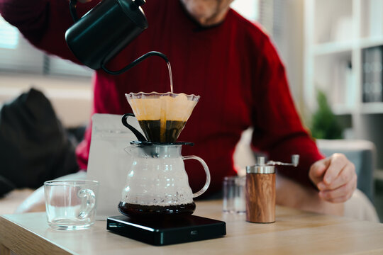 Senior man in a red sweater making pour over coffee with a glass dripper and kettle - Powered by Adobe
