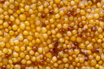 French Dijon mustard in a metal spoon, top view on mustard grains background. Gastronomy concept, organic food. Sauce. Slow rotation in a circle.	