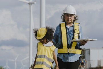 Grandmother and granddaughter in engineering uniforms work at wind farm that converts wind into...