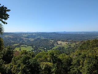 Sweeping view of lush green hills, farmland, and forests under a clear blue sky. A tranquil...