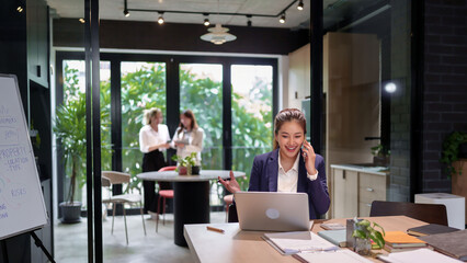 Asian Business Woman on Phone Call in Modern Office Professional at Desk Using Laptop Smiling Consulting Negotiating Communication Workplace