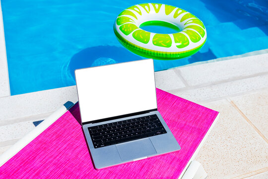 Laptop on a pink mat by a pool with a colorful float in a sunny setting
