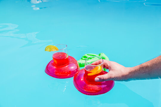Cherry pool float with drinks and a man's hand in a sunny pool