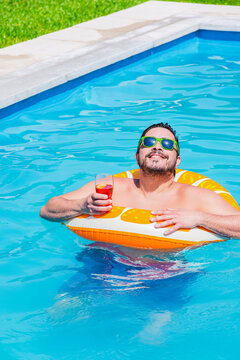 Man relaxing in a pool with a drink and pool float on a sunny day
