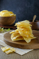 A stack of golden crispy potato chips on a wooden plate, with a rustic background. Traditional Asian snacks, ideal for use in food packaging, restaurant menus, snack promotions or culinary content