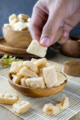 A hand picking up crispy tofu sticks, known as stik tahu, served in wooden bowls on a rustic setting. Perfect for promoting traditional Asian snacks, healthy foods, or culinary conten