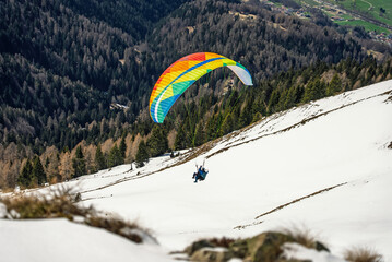 Paraglider soaring through the clouds above a snowy mountain range. Paraglider above clouds in a valley in the Dolomites, Alps. Paraglider takeoff on a snowy slope in the mountains. Italy, Pinzolo,.