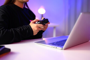 Close up of gamer holding a console controller while playing on a laptop