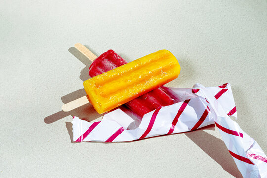 Close-up of mango and strawberry popsicles on a striped wrapper in sunlight