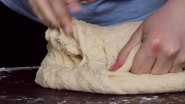female hands kneading yeast dough for bread on floured surface in home kitchen closeup strong pressing motion visible, concept of homemade baking, traditional cooking, food preparation industry