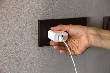A person is plugging a white USB charger into a black wall socket, symbolizing daily use of modern...