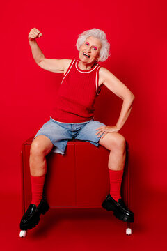 Joyful senior woman in red outfit posing with roller skates against a vibrant red background