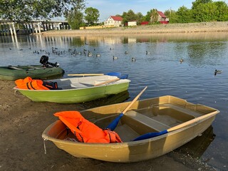 Three rowboats equipped with vibrant orange life jackets are moored by the riverbank.