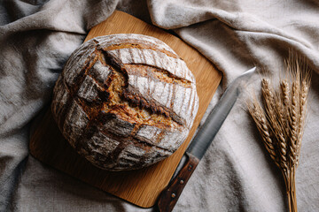 Freshly baked artisan bread on wooden board with knife and wheat  