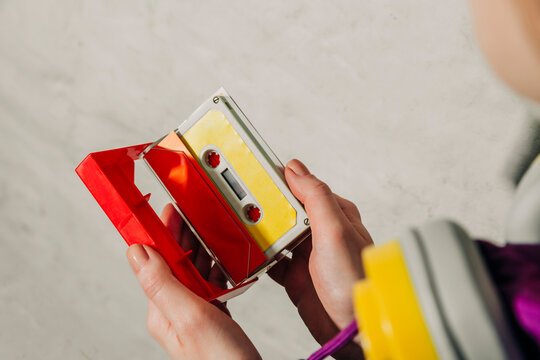 Person in 80s tracksuit holding an open cassette case indoors