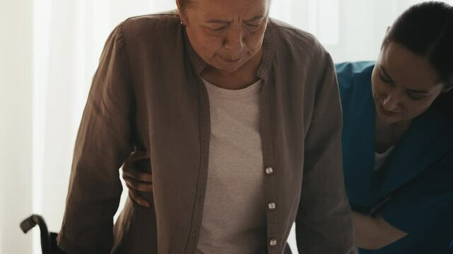Caring nurse helping elderly woman sit in wheelchair, mobility assistance, care