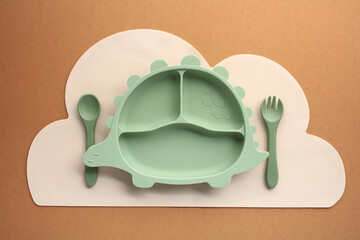 Green dinosaur silicone baby feeding set with plate, spoon, and fork on cloud placemat