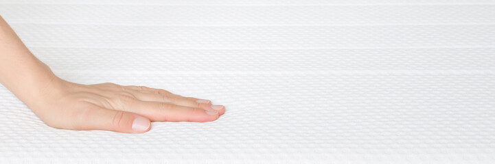 Young adult woman hand touching clean white orthopedic mattress. Checking hardness and softness. Closeup. Wide banner. Empty place for text. Front view.
