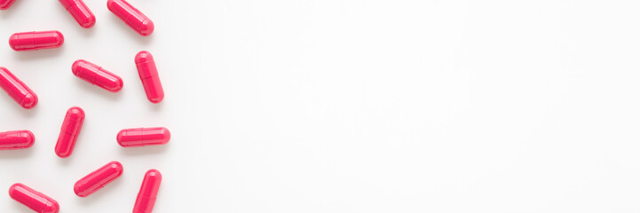 Red capsule pills for improve of iron level in blood on white table background. Closeup. Wide banner. Empty place for text. Top down view.