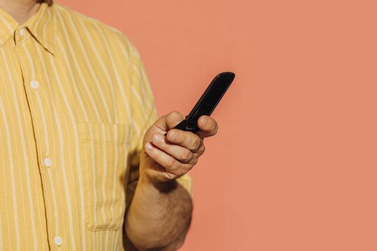 Mid adult man in yellow shirt holding a flip phone against an orange background